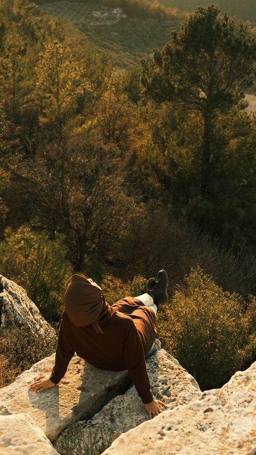Free Person relaxing on rocky overlook, surrounded by lush trees in serene outdoor setting. Stock Photo