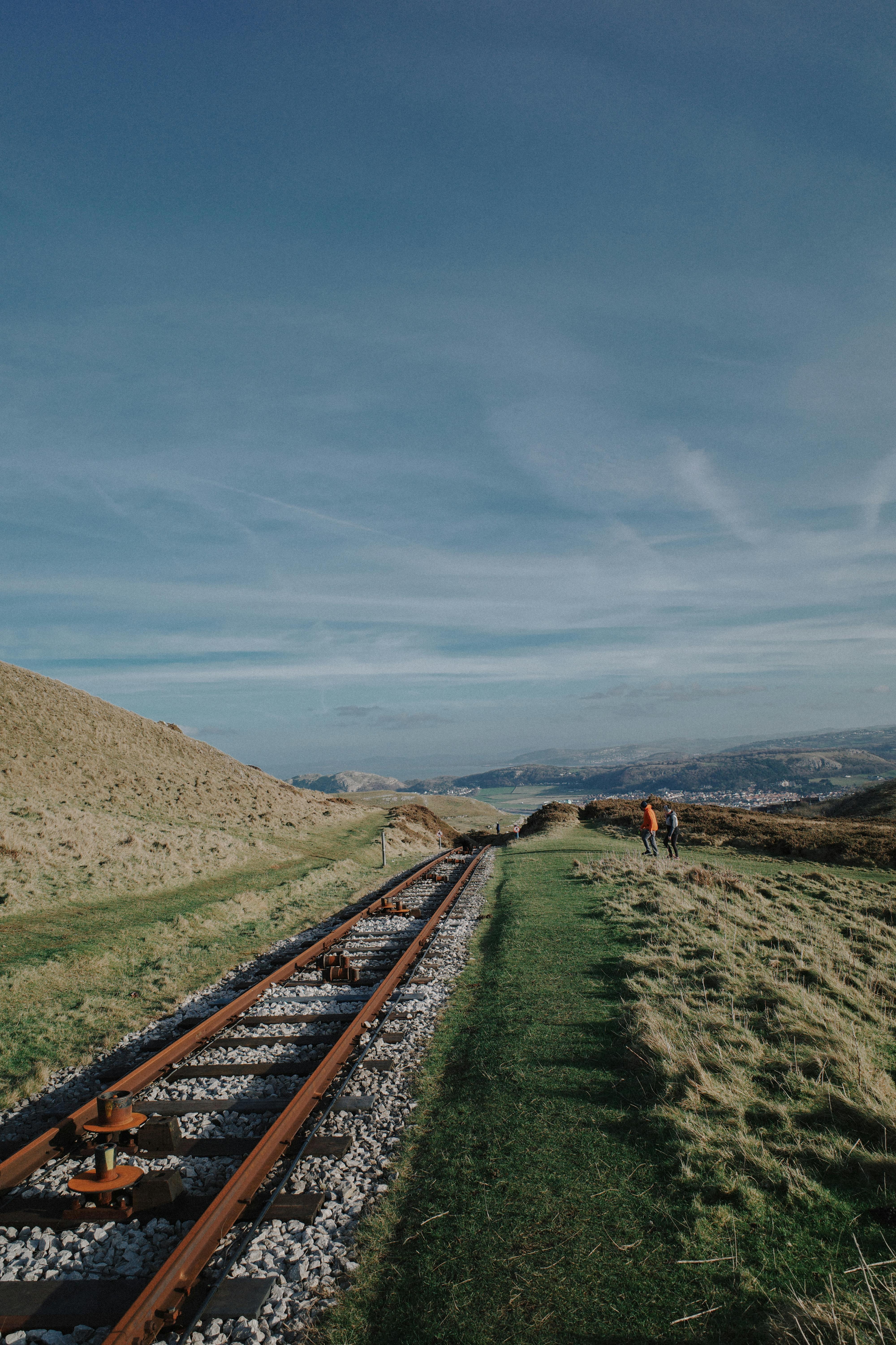 Explore the tranquil beauty of Welsh mountains along a scenic railtrack under a clear blue sky.