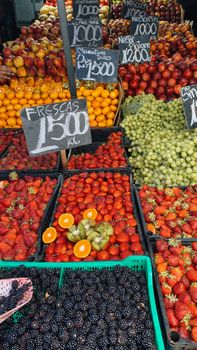 Colorful array of fresh fruits in an open-air market stall with price signs.