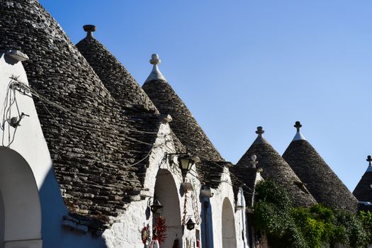 Explore the iconic trulli houses under a clear blue sky in Alberobello, Italy, a UNESCO World Heritage site.