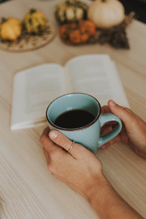 Person, Die Tasse Kaffee Neben Einem Offenen Buch Hält