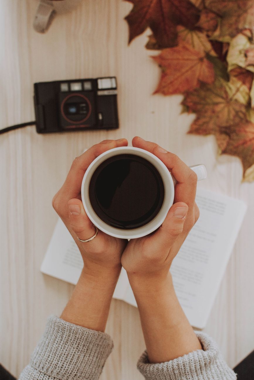 Cup of coffee held over a book with autumn leaves and a vintage camera.. coffee, held, over