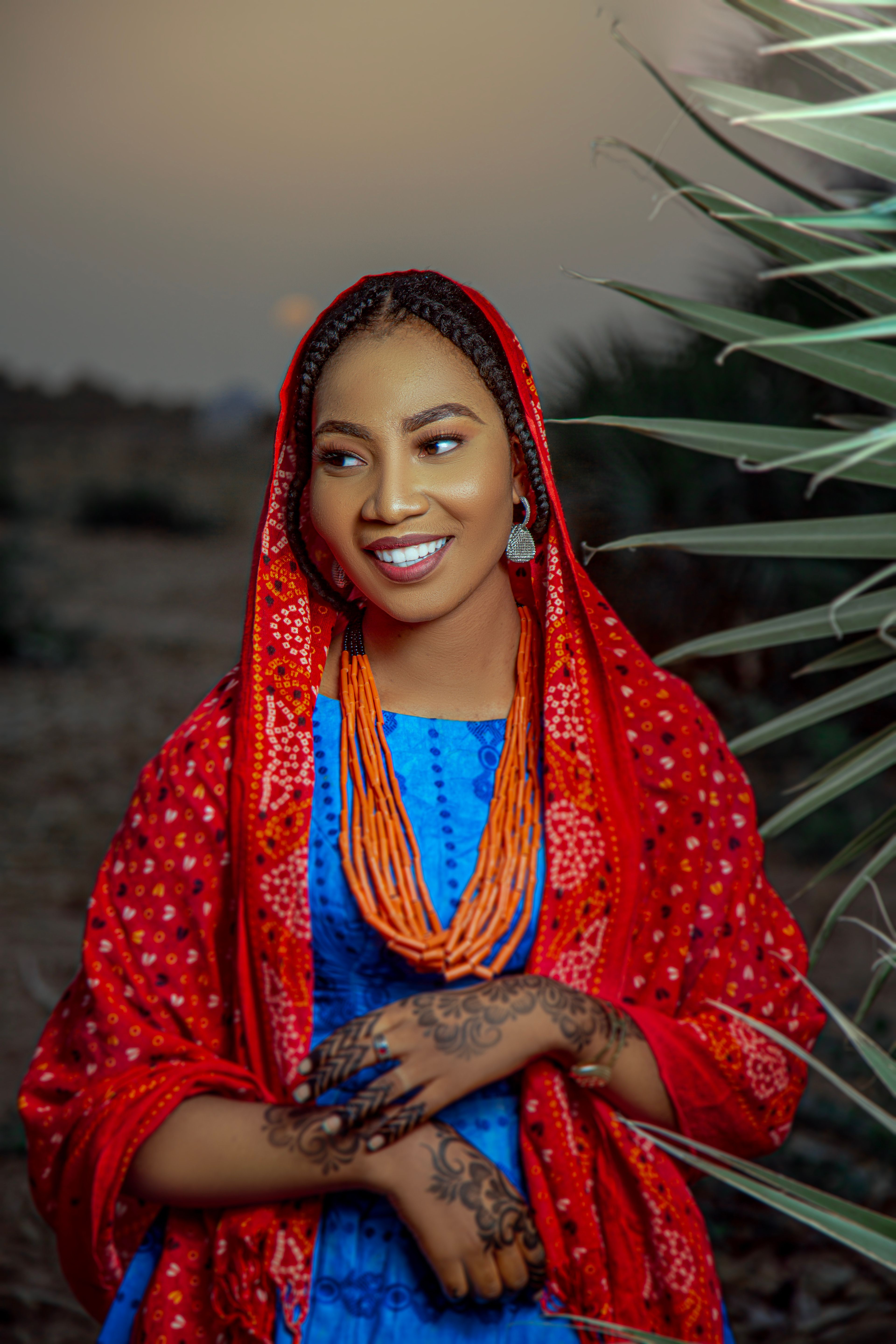 Vibrant outdoor portrait of a smiling woman in traditional attire with henna designs.