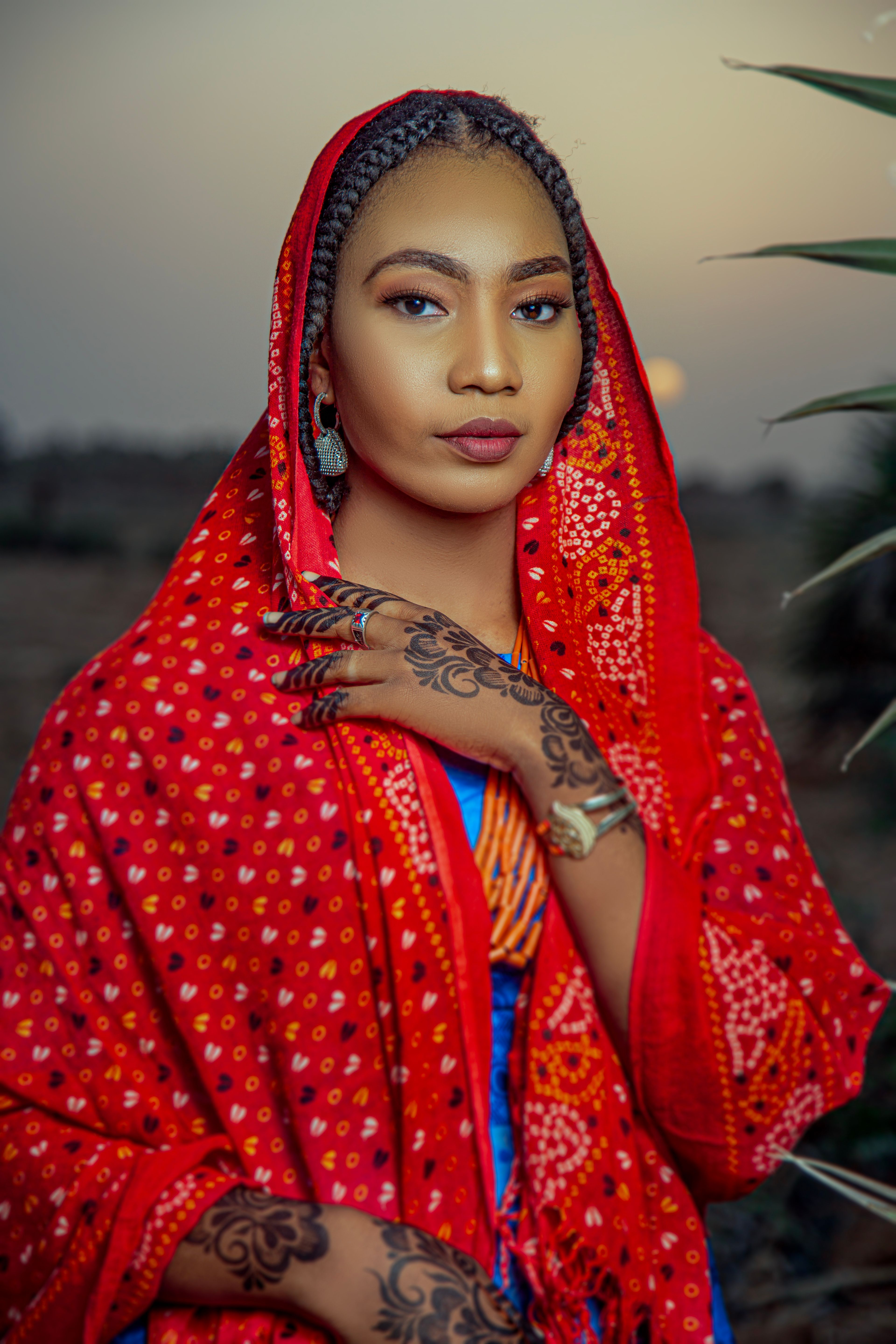 Young woman in vibrant red traditional attire with henna hand art at sunset.