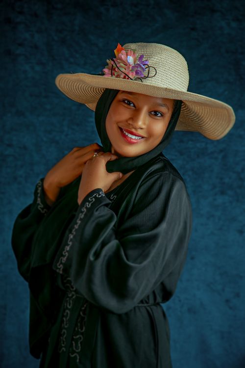 Free Portrait of a woman in a black hijab and floral hat, smiling confidently. Stock Photo