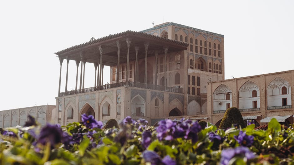 A beautiful view of Ali Qapu Palace in Esfahan, Iran with vibrant purple flowers in the foreground.