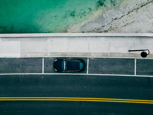 Overhead view of a car in a single bay beside turquoise water. Photo by Maheshwar Reddy on Pexels