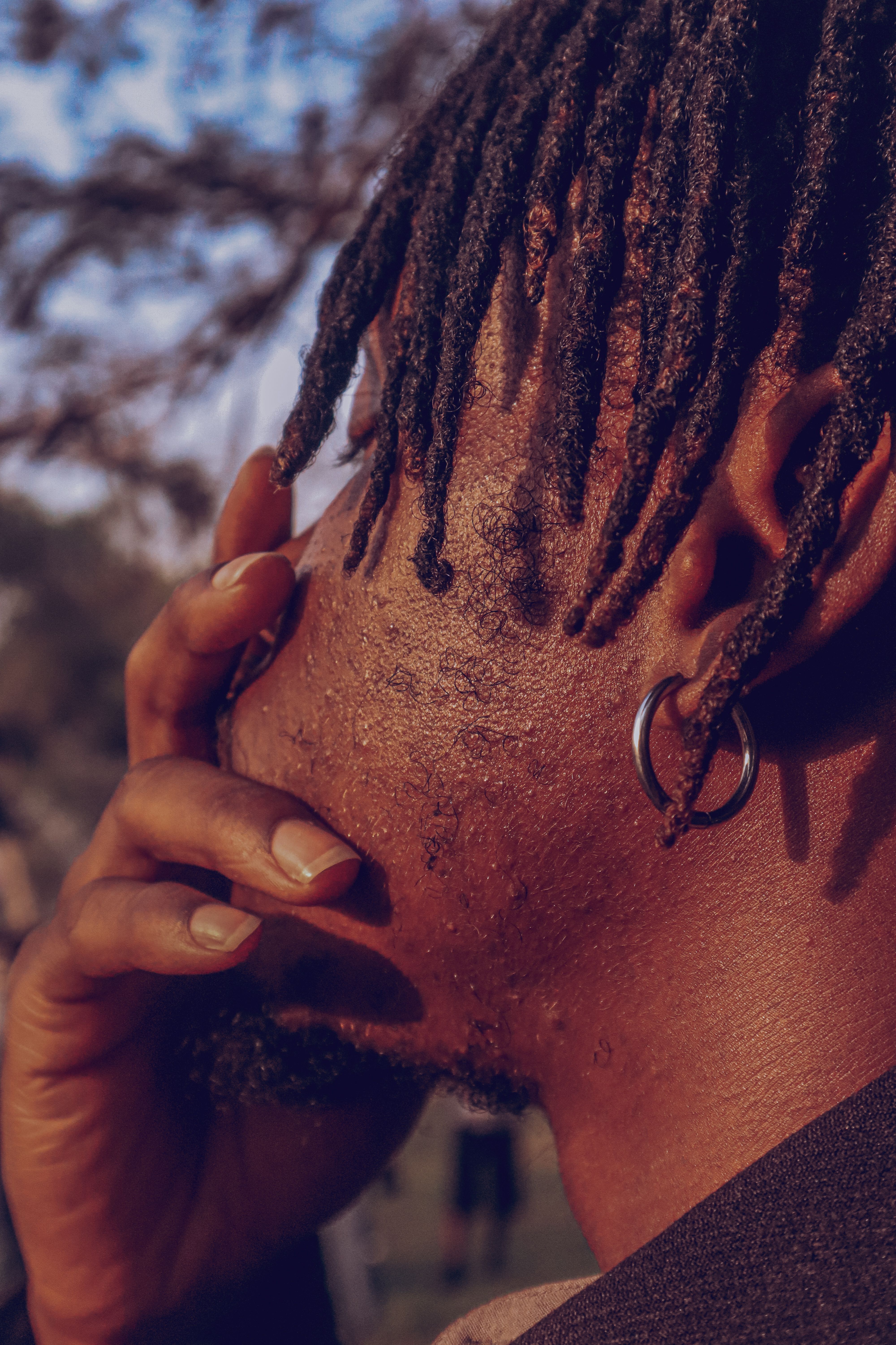A contemplative man outdoors with dreadlocks and an earring, captured in warm light.