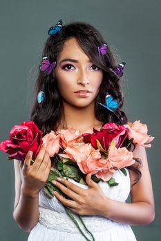 A young woman with butterflies in her hair, holding roses against a gray backdrop in a studio.
