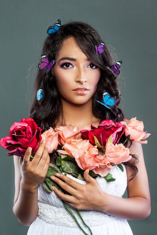 Free A young woman with butterflies in her hair, holding roses against a gray backdrop in a studio. Stock Photo