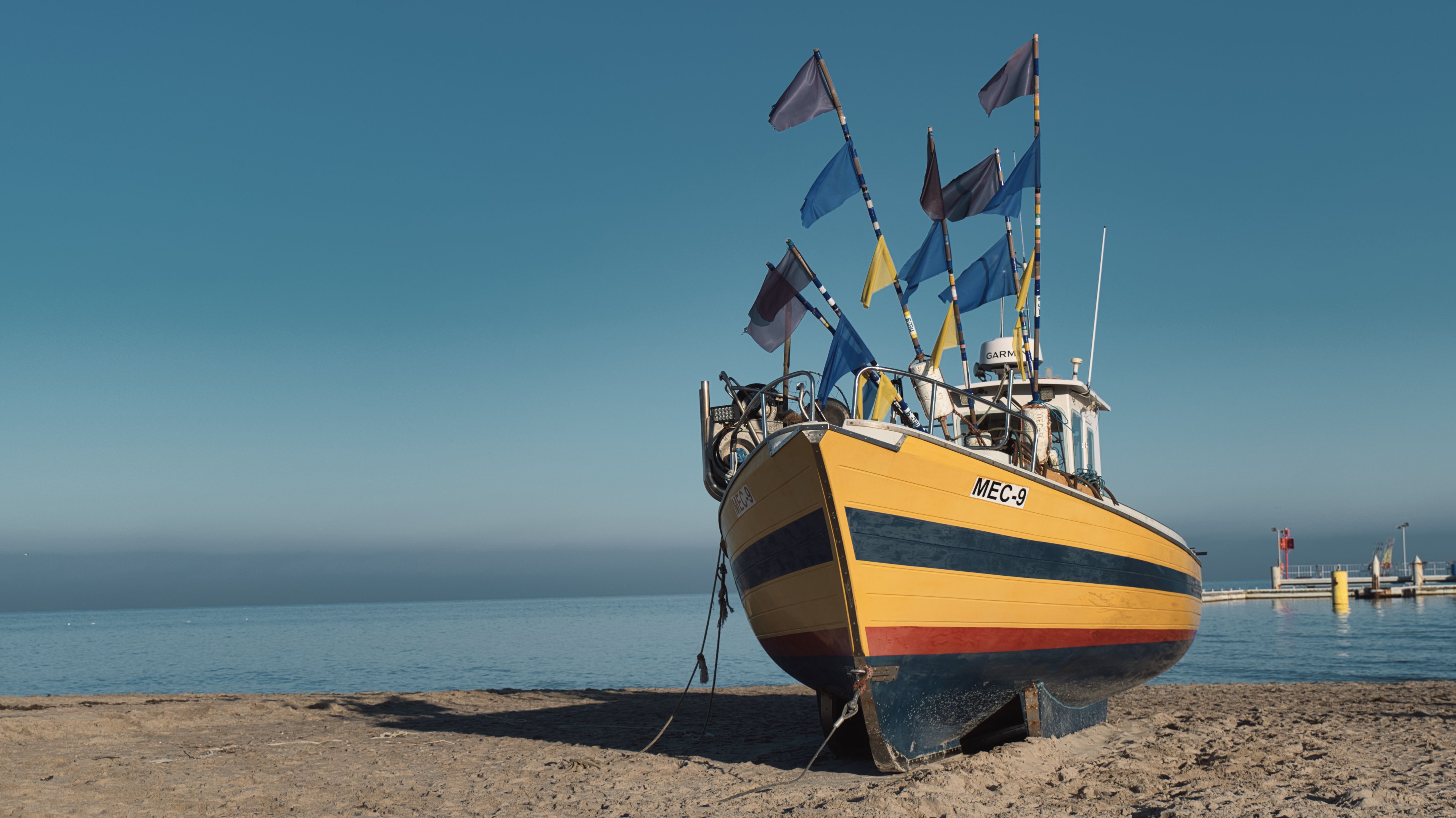 Vibrant fishing boat with flags on a sunny beach in Gdynia, Poland.