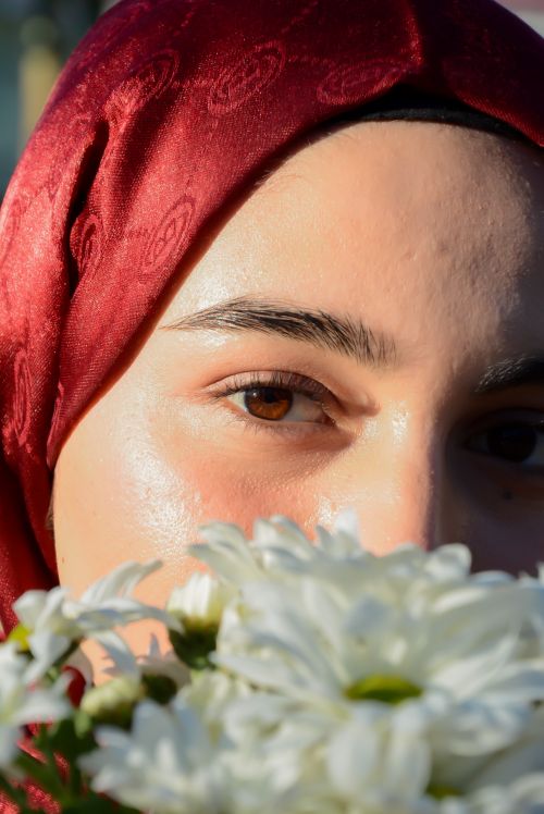 Free Close-up portrait of a woman wearing a red hijab, holding white flowers. Stock Photo