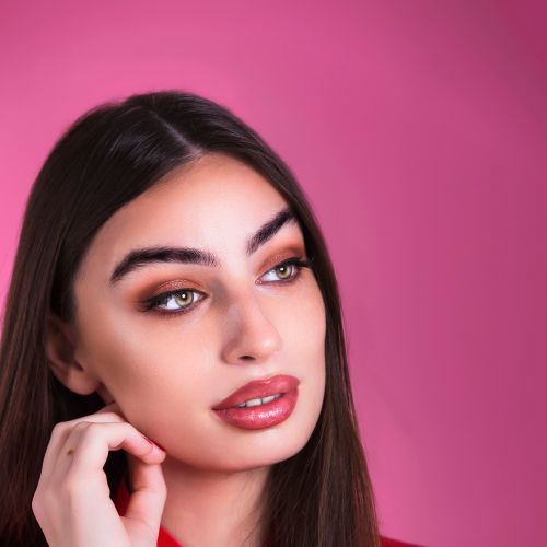 Free Portrait of a woman with makeup against a pink backdrop, conveying elegance. Stock Photo