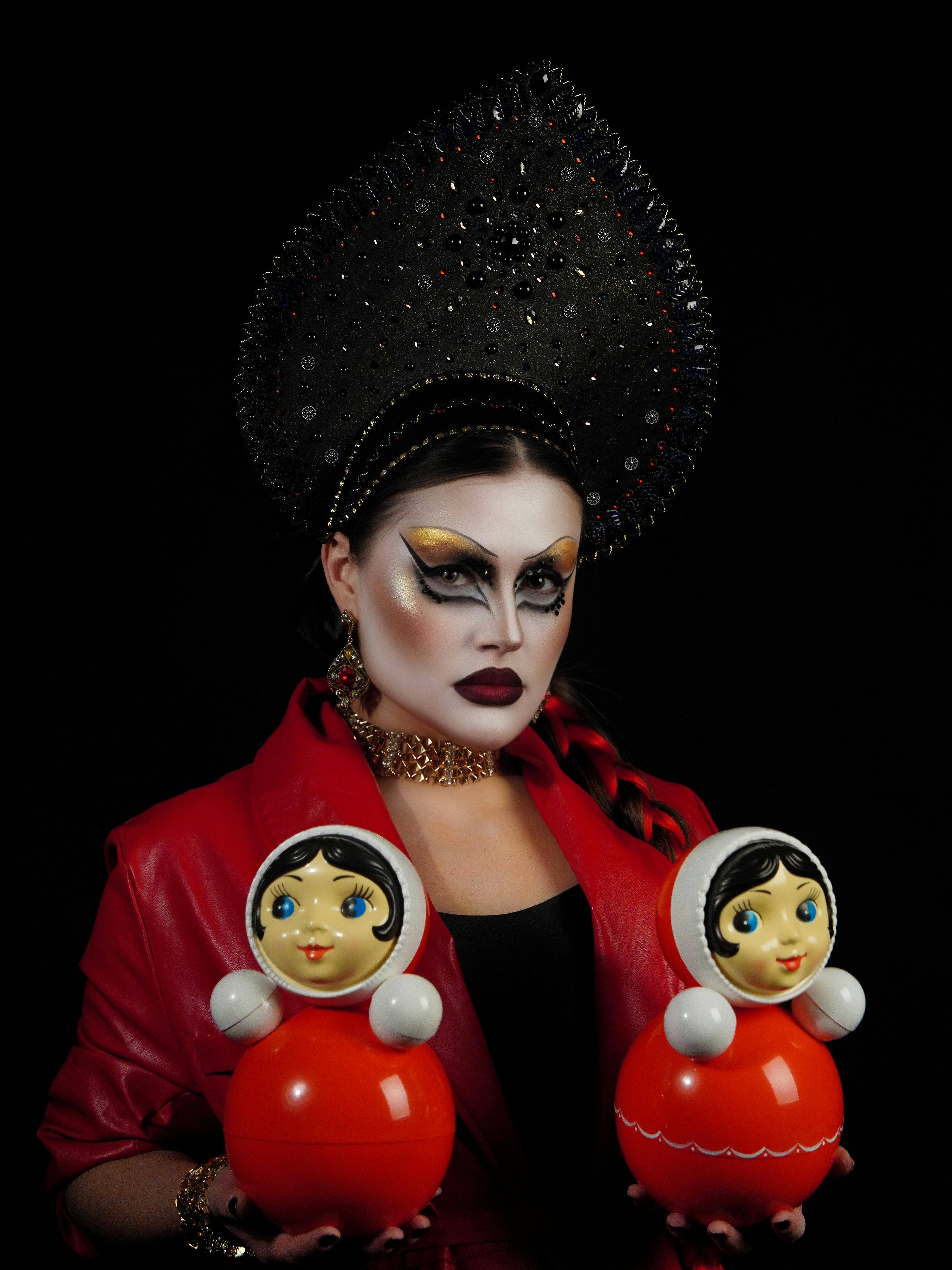 Free Striking image of a woman in theatrical makeup, adorned in traditional headdress, holding dolls. Stock Photo