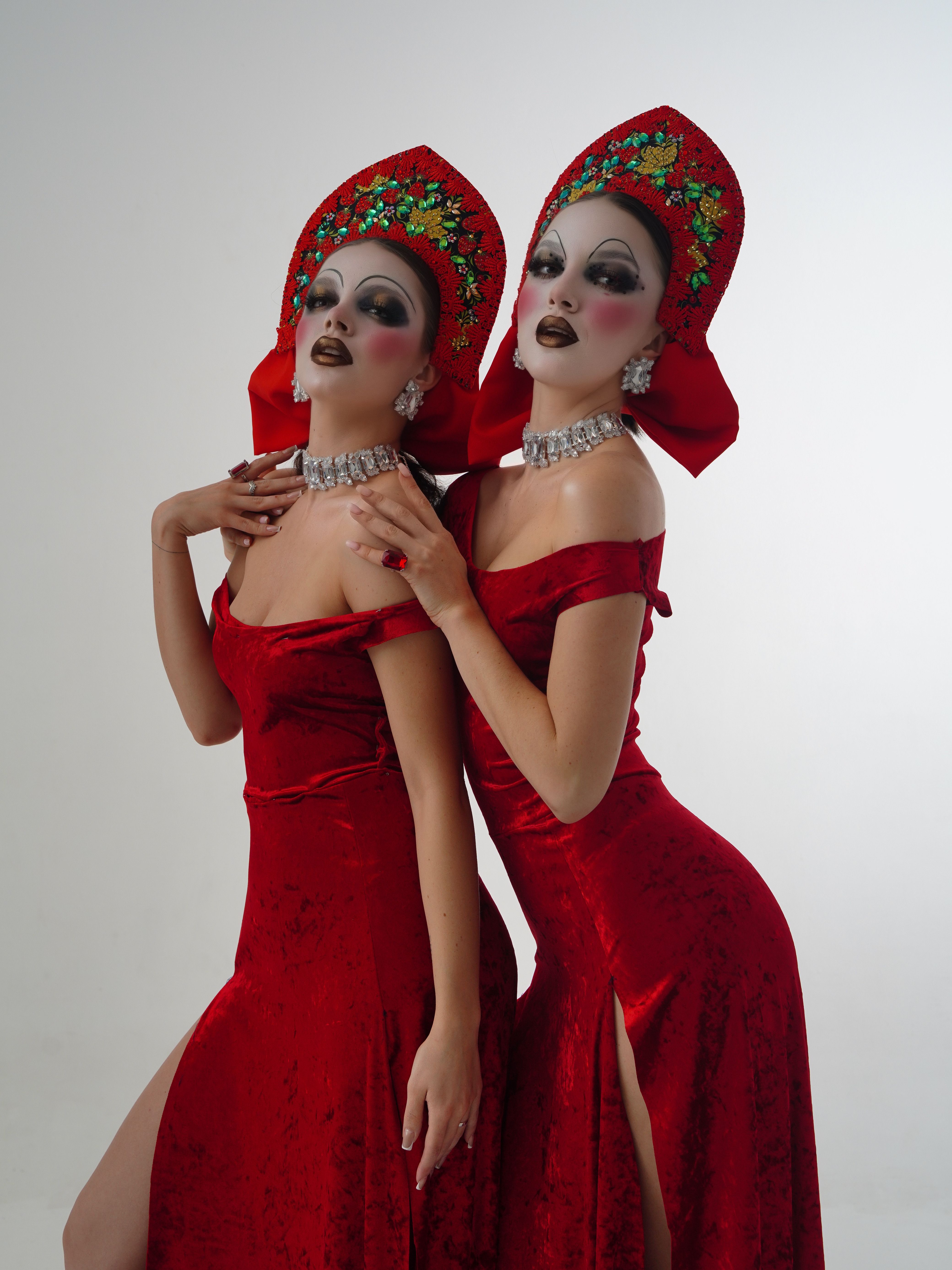 Two performers in red velvet dresses with dramatic makeup and traditional headdresses.