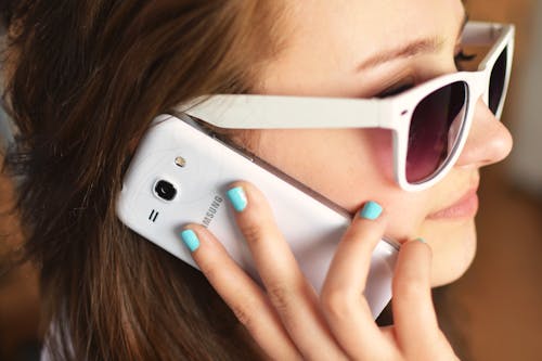Free Smiling Woman Wearing Sunglasses While Talking on White Samsung Smartphone Stock Photo
