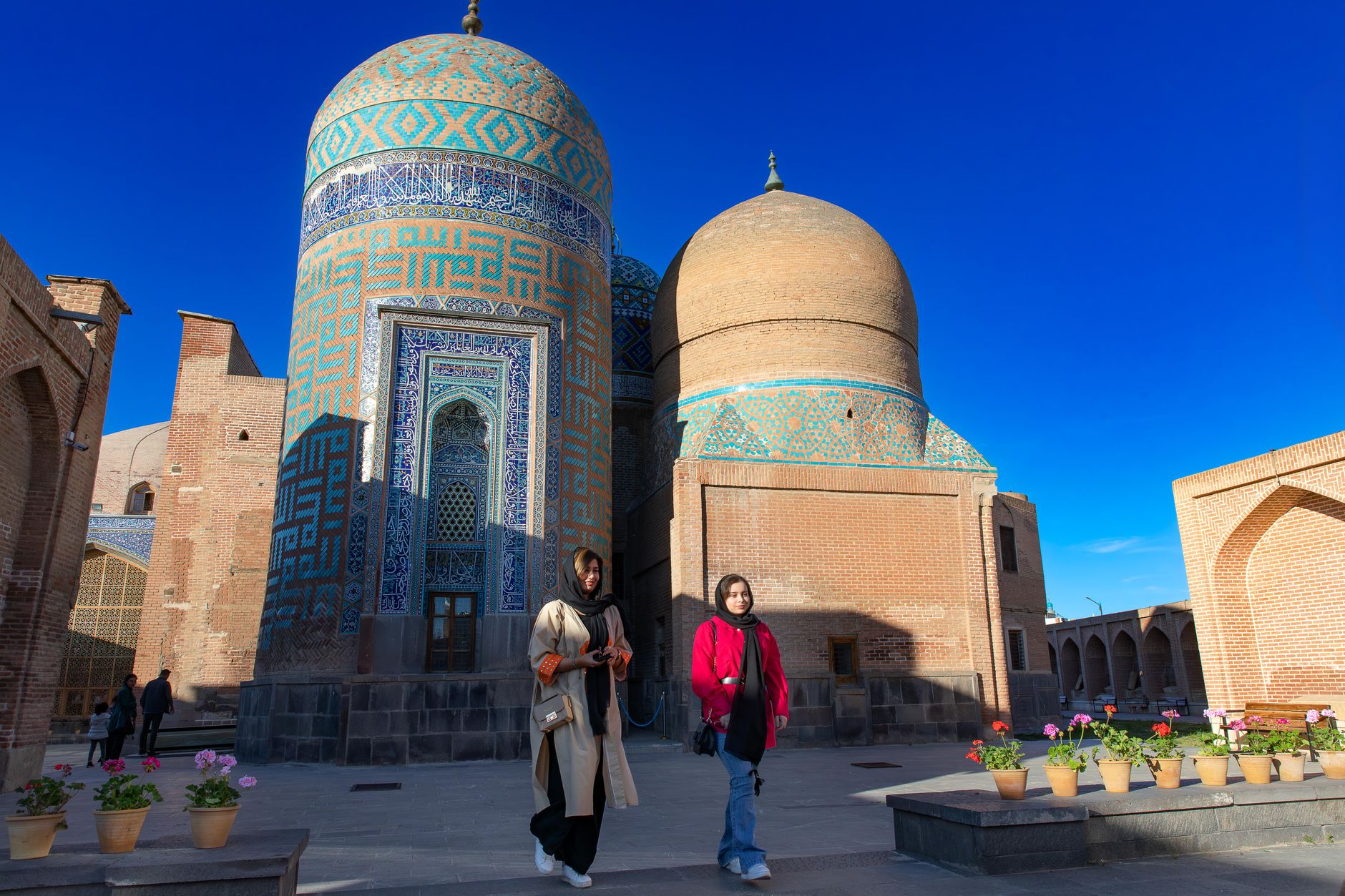 Two women walking at the historic Sheikh Safi al-Din Shrine in Ardabil, showcasing Islamic architecture.