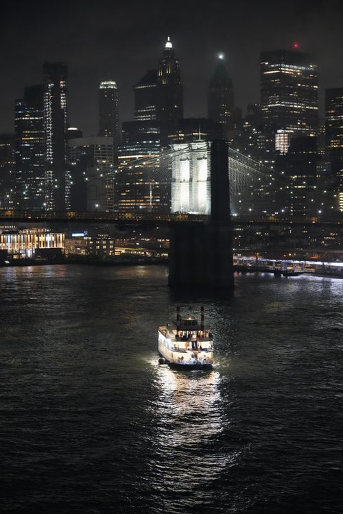 Free A boat sails under the iconic Brooklyn Bridge with the New York City skyline illuminated at night. Stock Photo