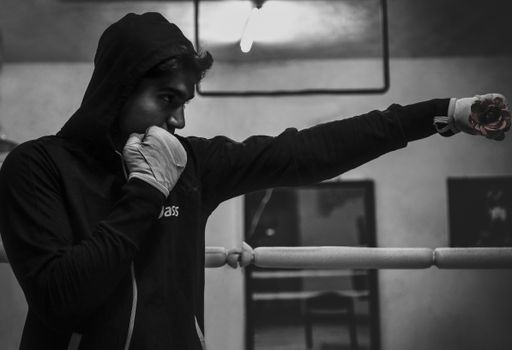 Black and white image of a boxer in a hoodie practicing punches in a boxing ring.
