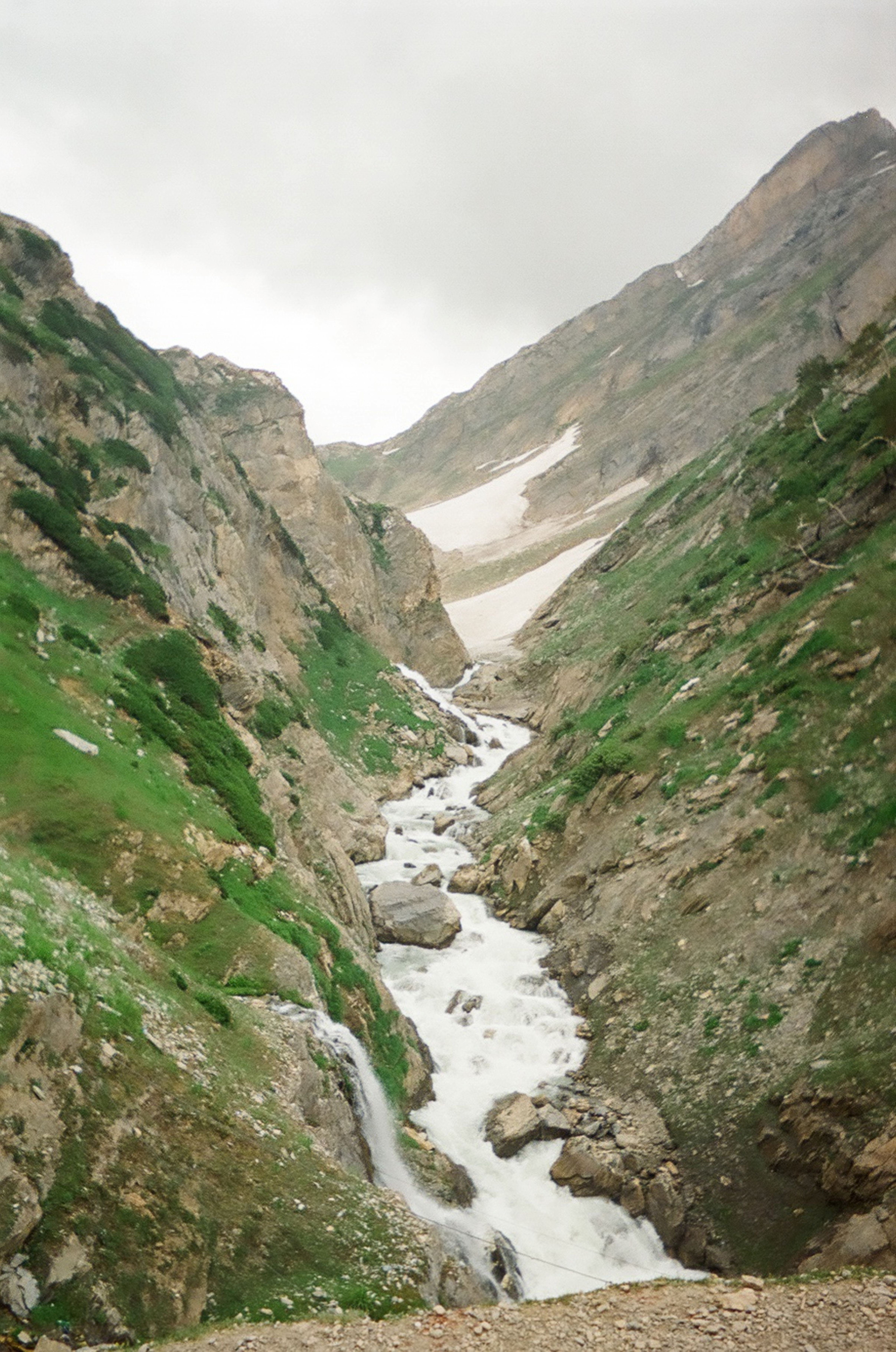 A breathtaking view of a mountain stream cascading through a rocky valley surrounded by lush greenery.