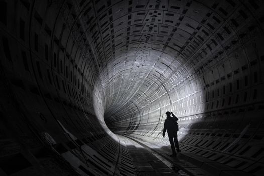 Mysterious silhouette of a person walking through a dimly lit, futuristic underground tunnel.