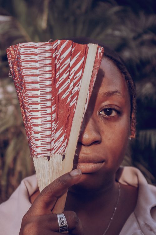 Free Close-up portrait of woman holding a traditional red patterned fan outdoors. Stock Photo
