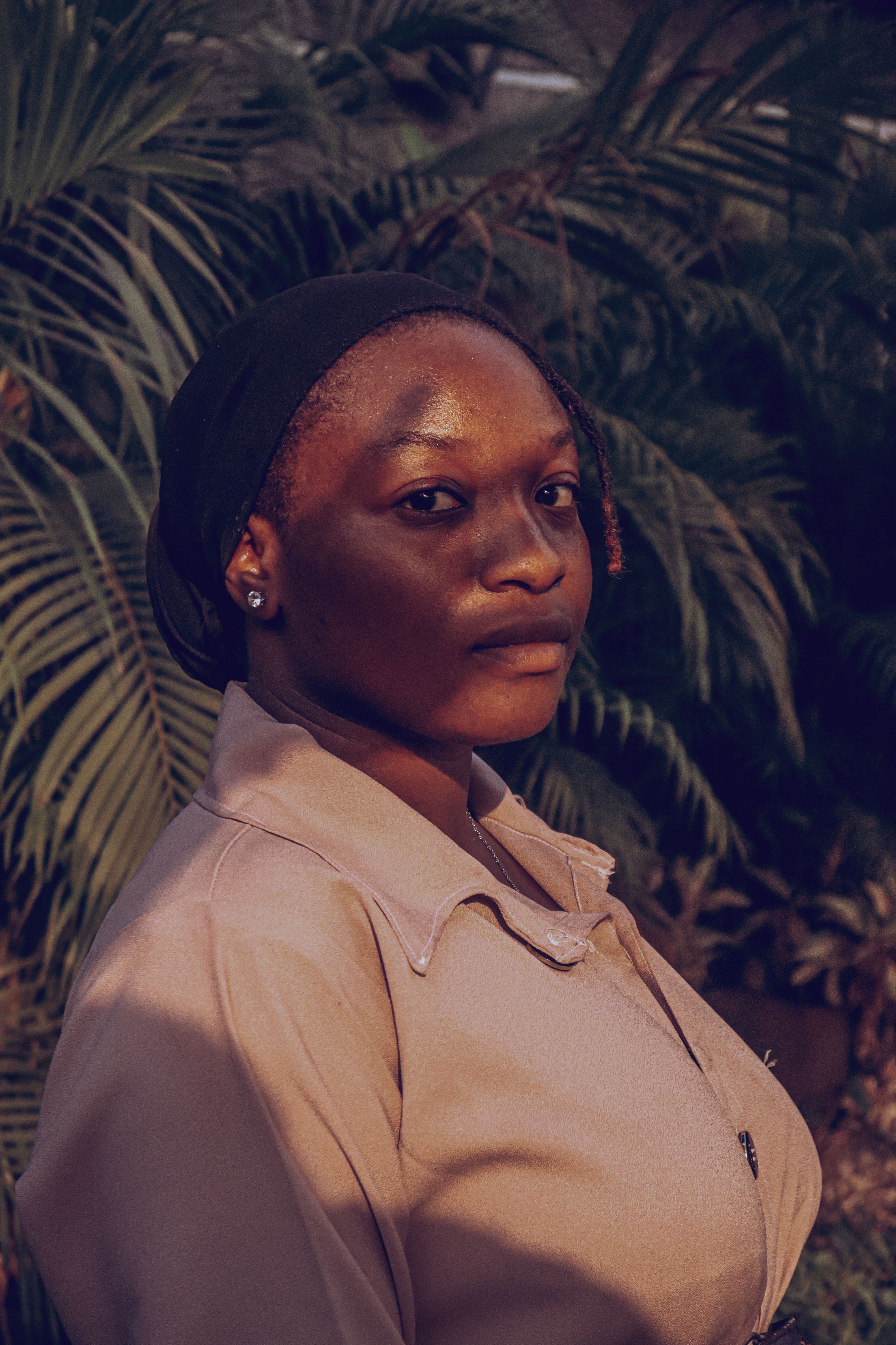 A thoughtful young woman stands amidst tropical foliage, bathed in warm evening light.