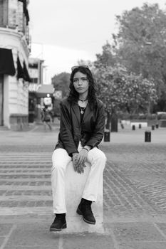 A stylish woman in a leather jacket sitting on a city street in black and white.