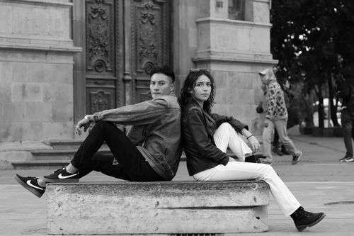Free Stylish young adults in black and white photo sitting on a bench in an urban setting, posing fashionably. Stock Photo