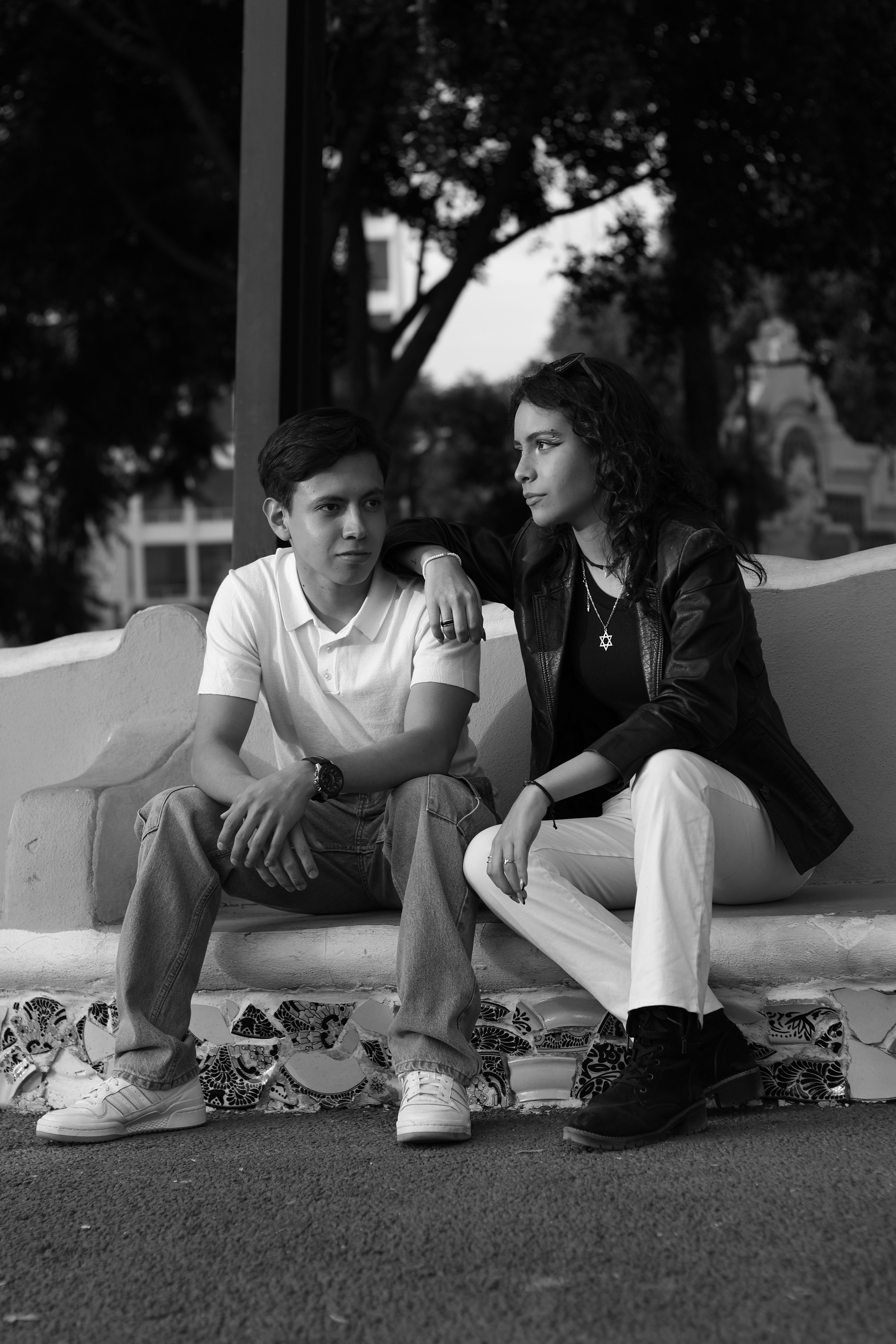 Black and white portrait of a stylish young couple sitting outdoors on a bench.