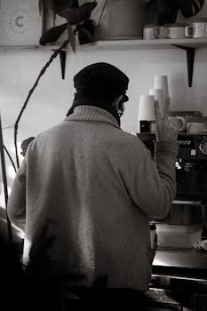Barista in winter clothing preparing coffee in a cozy indoor café setting.