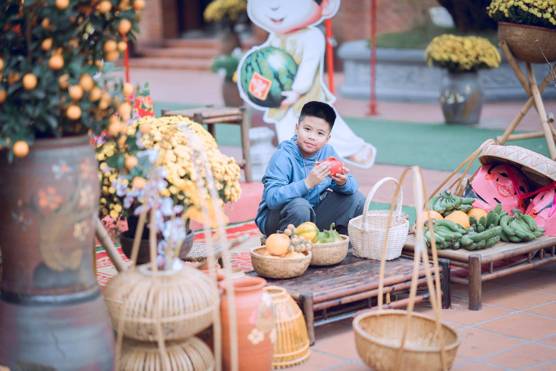 Young boy in a vibrant market setting surrounded by fruits and decorative items.