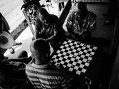 Men engaged in an outdoor checkers game in a lively, urban setting. Captured in black and white.