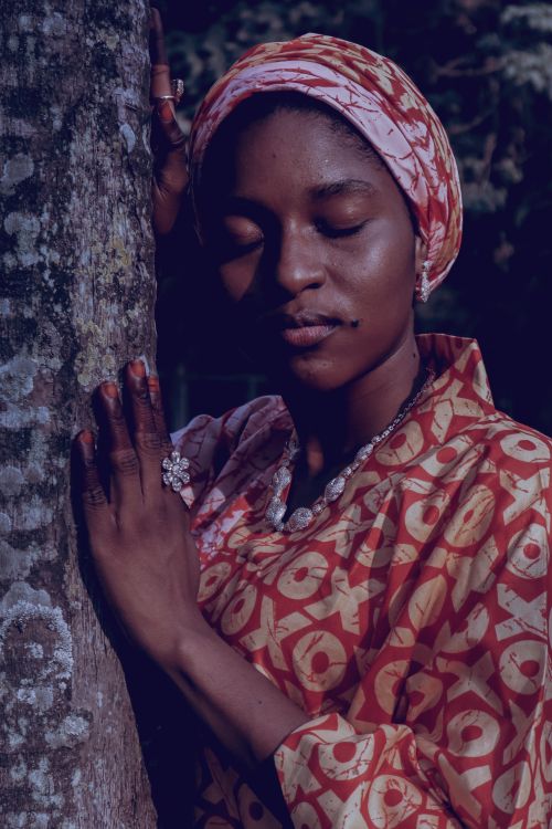 Free Woman in vibrant African dress rests peacefully by tree, creating a culturally rich and serene scene. Stock Photo