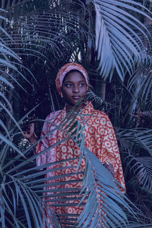 Free Portrait of a woman in traditional clothing surrounded by lush palm leaves. Stock Photo