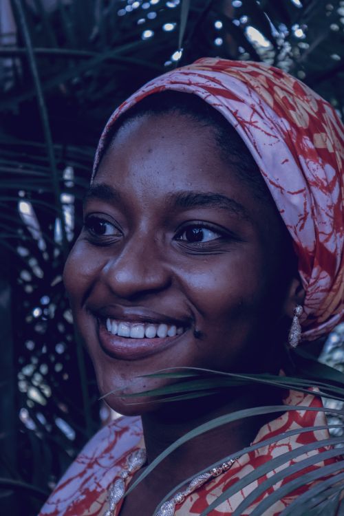Free Portrait of a joyful woman wearing a colorful headscarf, surrounded by greenery. Stock Photo
