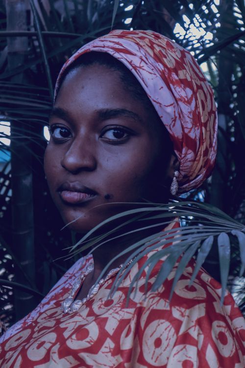 Free A serene portrait of a woman in traditional African attire surrounded by lush green foliage. Stock Photo