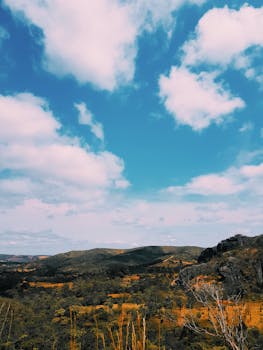 Beautiful rural landscape featuring hills and vibrant sky with fluffy clouds, perfect for travel inspiration.