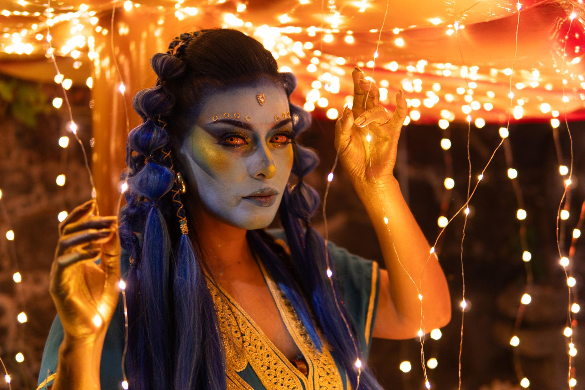 A captivating portrait of a woman with blue skin and gold details in a mystical setting with lights.