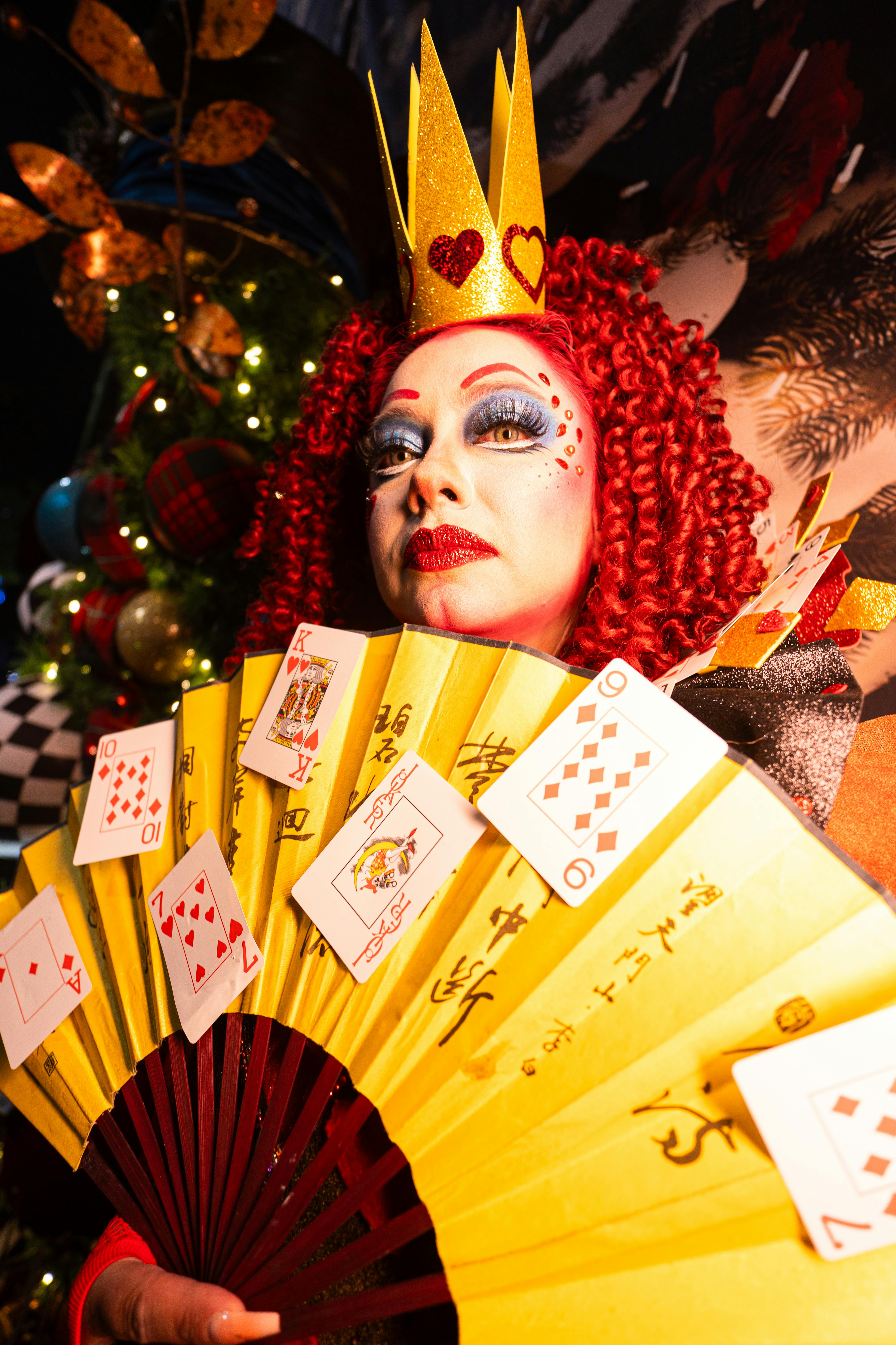 Free Colorful theatrical cosplay of Queen of Hearts with artistic makeup and playing cards, inspired by Alice in Wonderland. Stock Photo