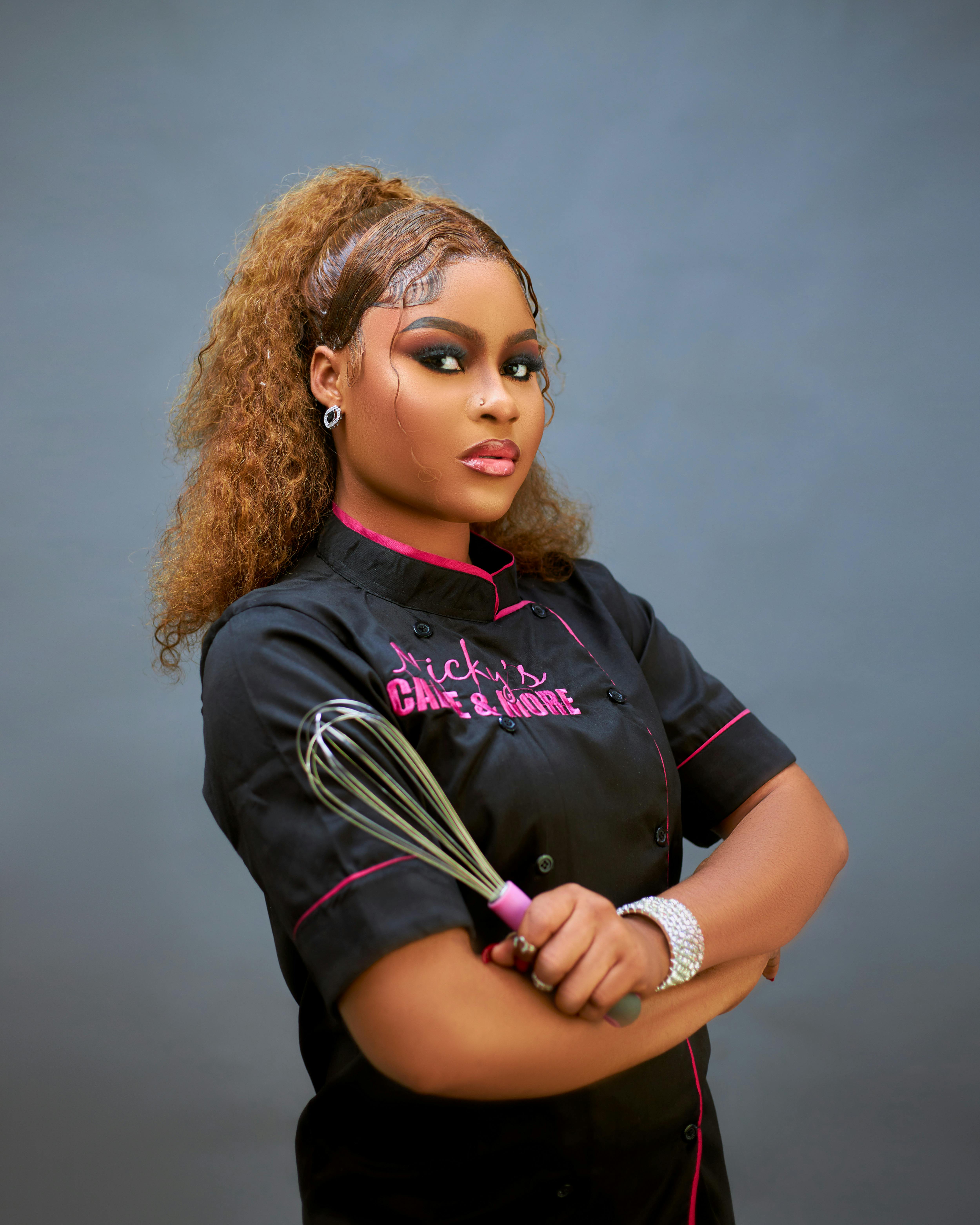Culinary professional in black chef's attire holding a whisk, showcasing confidence and expertise.