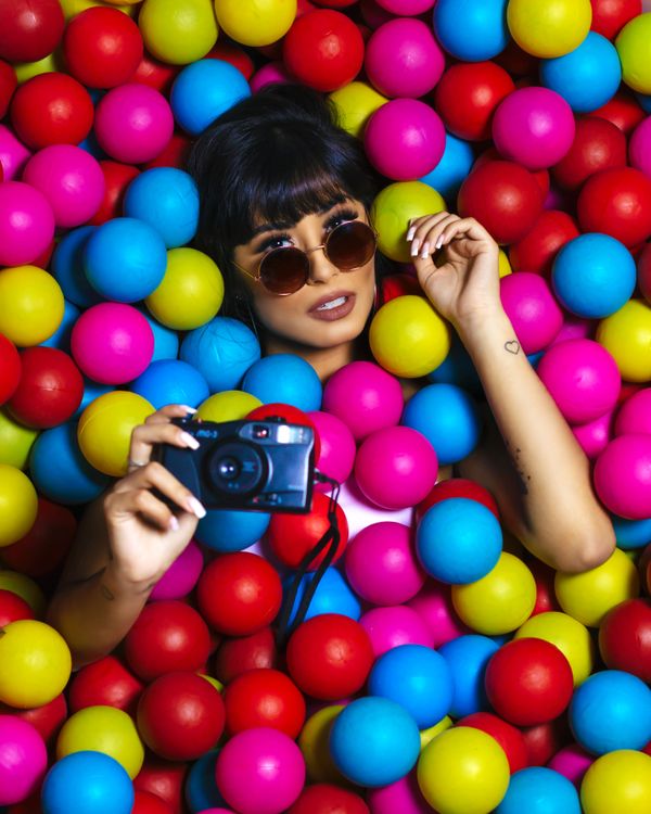 Creator in sunglasses holding a camera among colourful balls — photo by Cleyton Ewerton on Pexels
