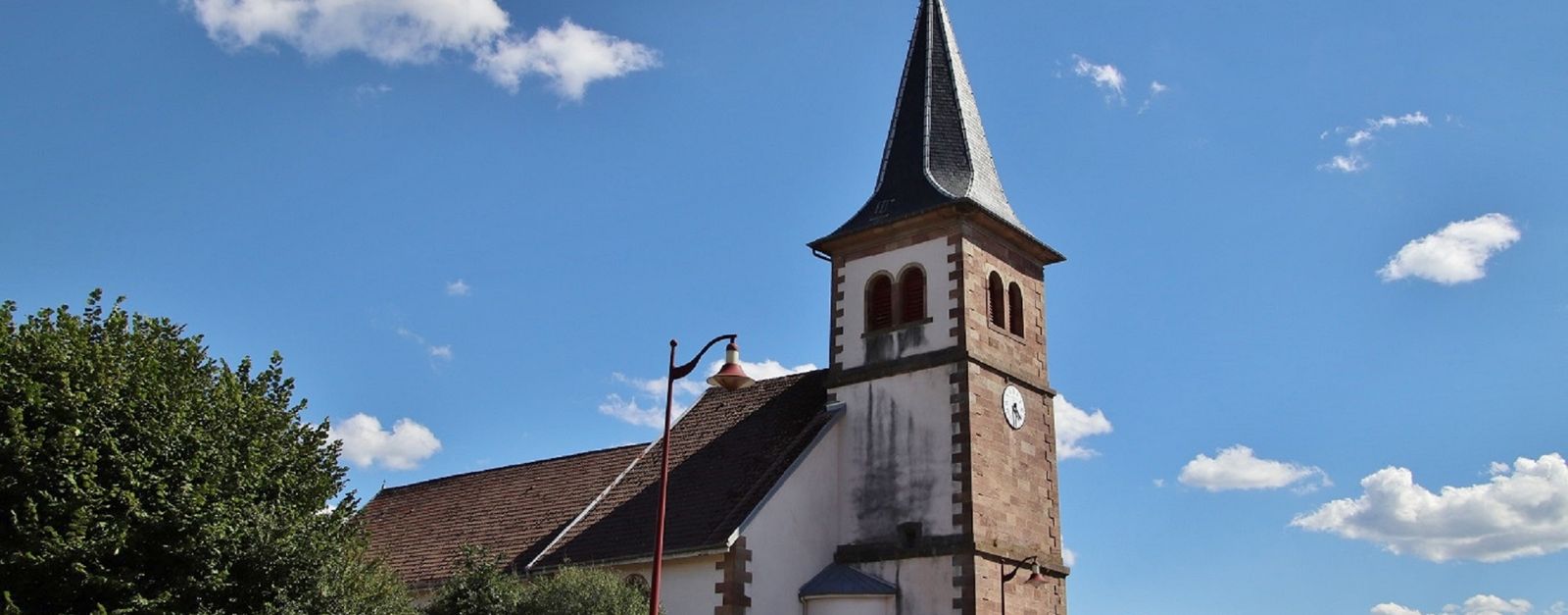 Beautiful historic church in Charmes-sur-Rhône against a clear blue sky with fluffy clouds.
