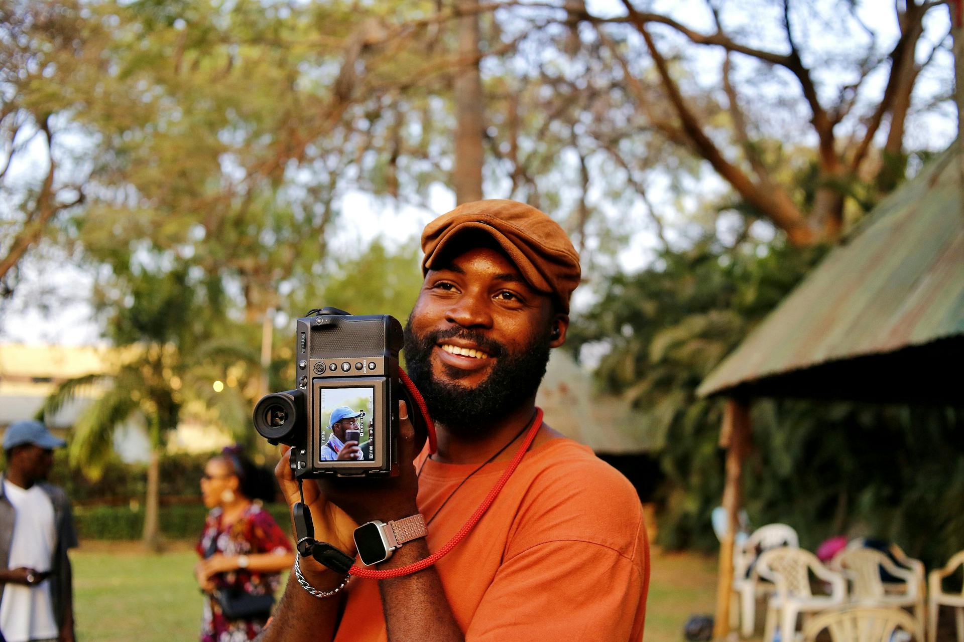 Smiling African photographer with camera outdoors in Abuja park. Captured amidst nature.