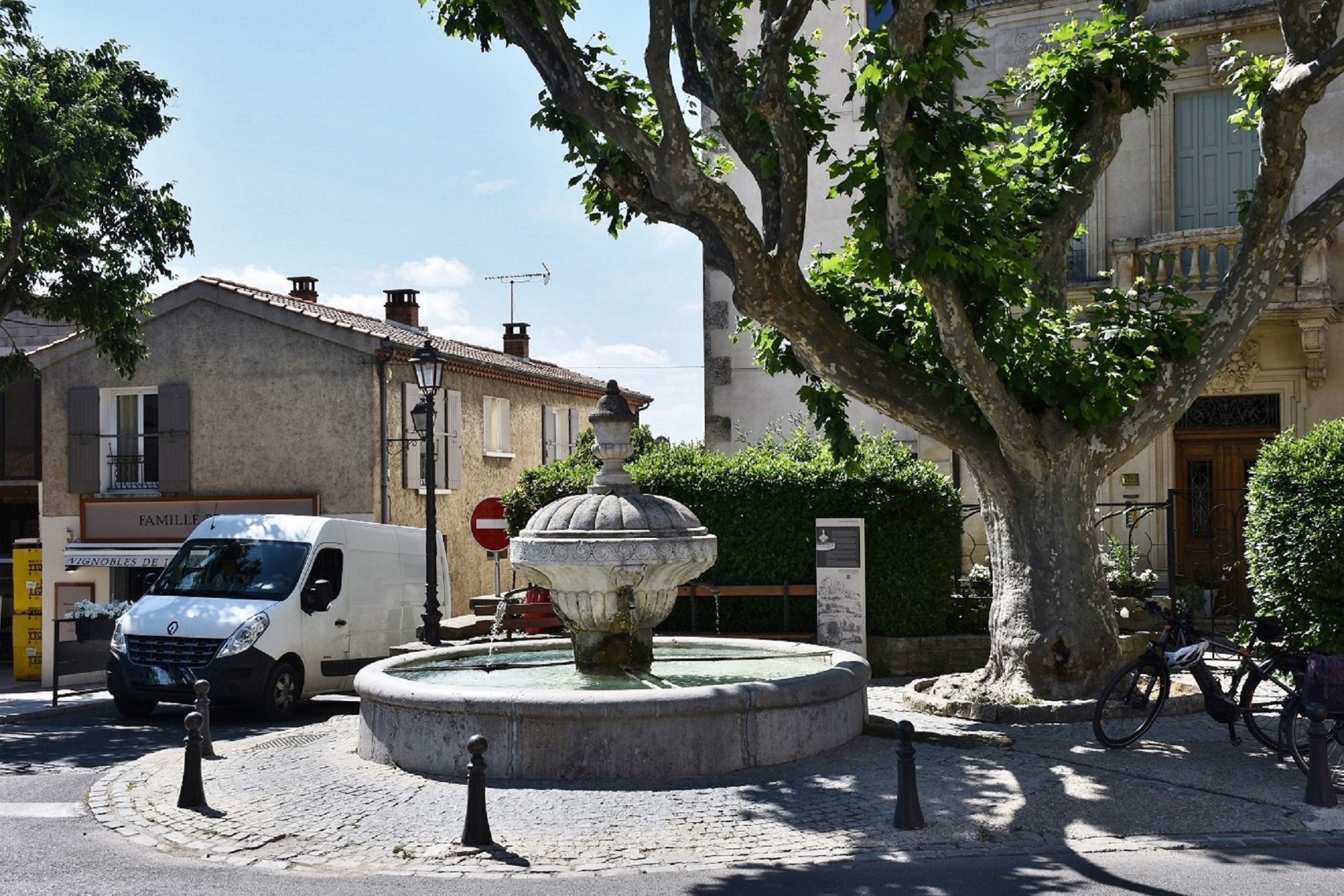 Picturesque street scene featuring a water fountain and tree in Châteauneuf-du-Pape, France.