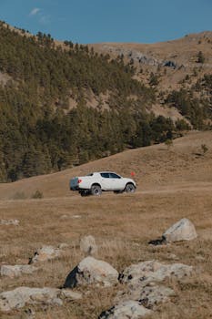 White off-road vehicle traversing a scenic mountainous landscape under a clear blue sky.