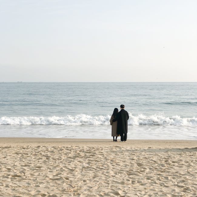 A couple enjoying a peaceful walk on a serene beach with gentle waves.