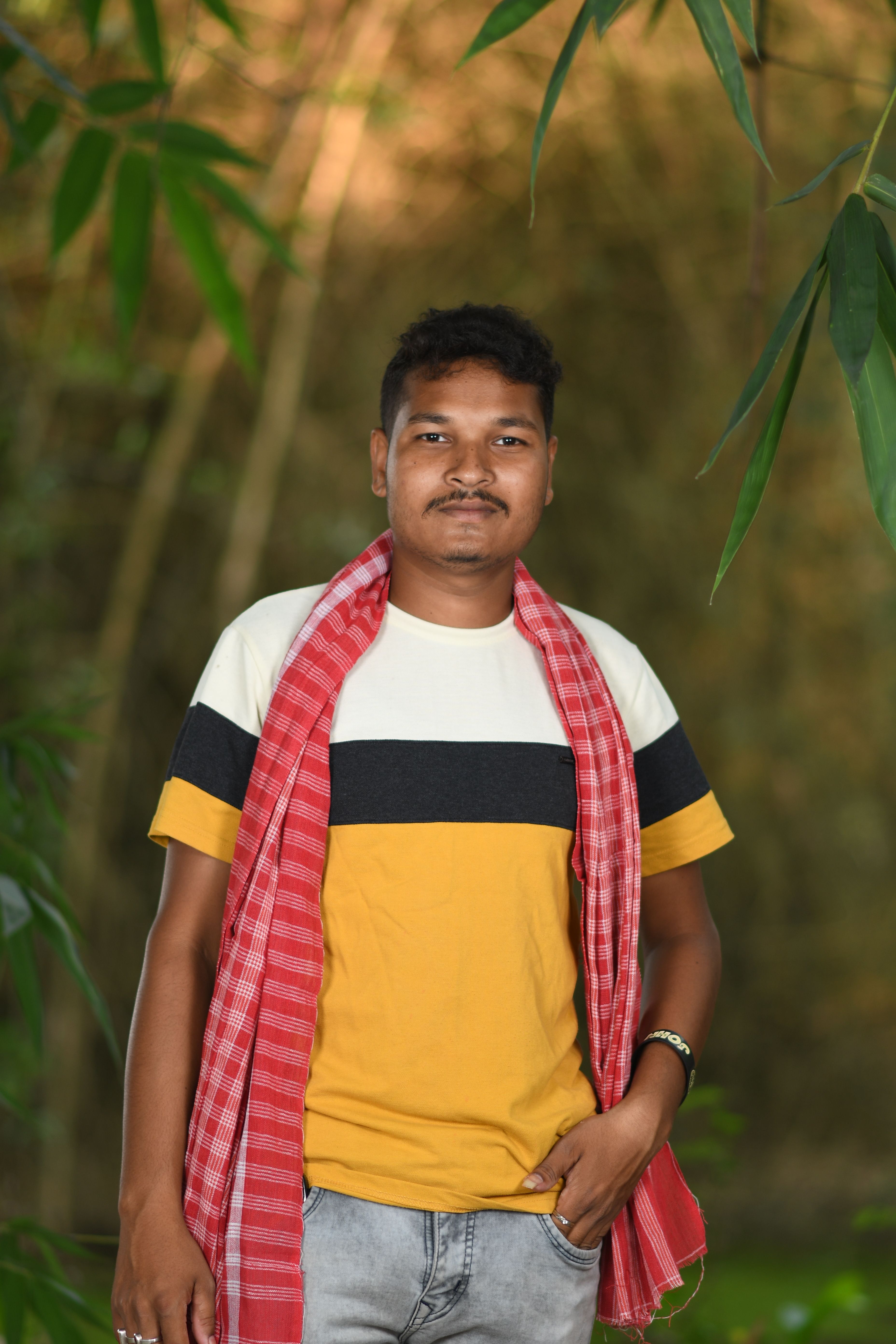 A young man poses confidently amidst vibrant green bamboo in a natural setting.
