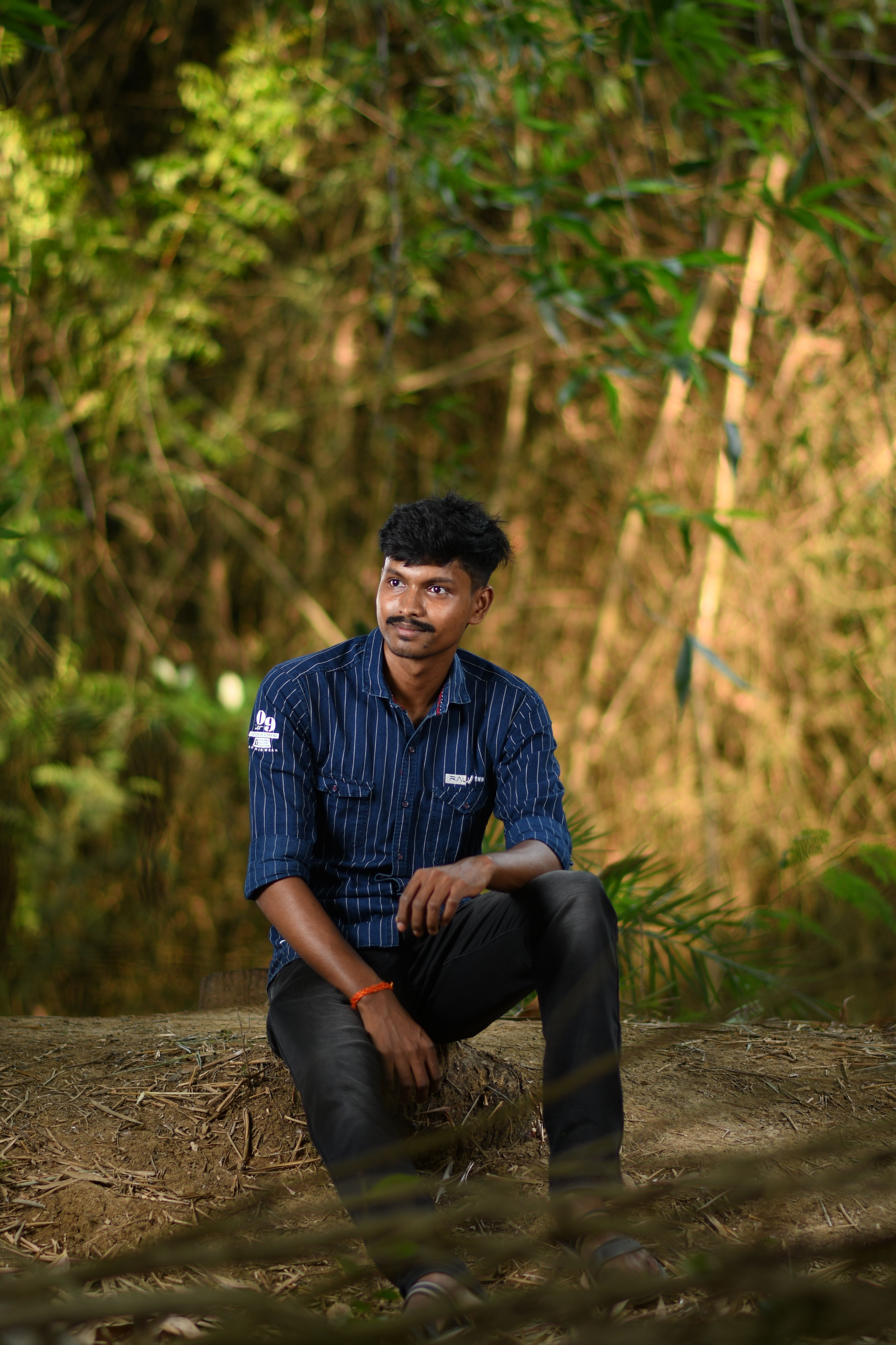 A man sitting on a log outdoors, surrounded by lush green foliage.