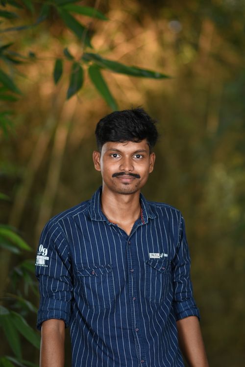 Free Young man smiling while standing in a lush forest, wearing a blue shirt. Stock Photo